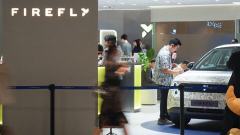 Thai illustrator Tent Katchakul decorates a white Firefly EV inside the showroom as visitors pass by.