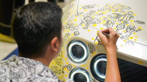 Close-up of Thai illustrator Tent Katchakul adding black and yellow artwork to the hood of a white Firefly EV.