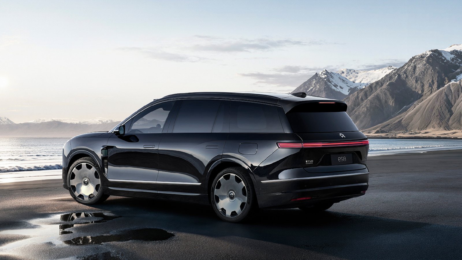 Rear three-quarter view of a black third-generation Nio ES8 beside the water, with snow-capped mountains in the background.