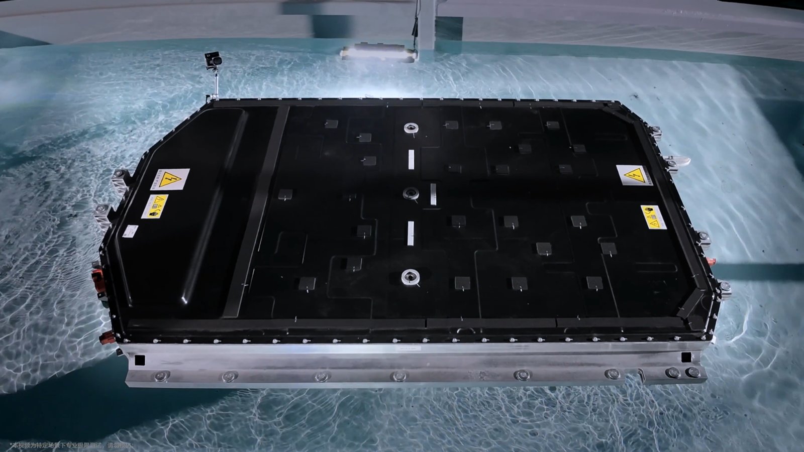 A black Li Auto battery pack with yellow high-voltage warning labels sits submerged in a pool of clear water during a water immersion test.