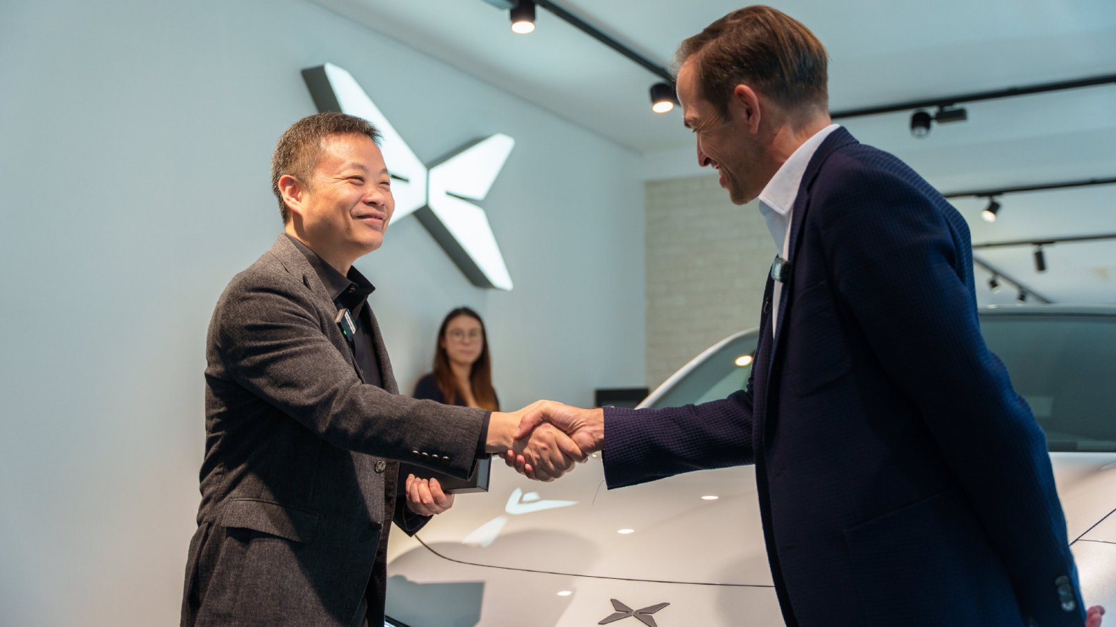 Xpeng chairman and CEO He Xiaopeng, left, shakes hands with a man beside a white Mona L03 in a showroom.