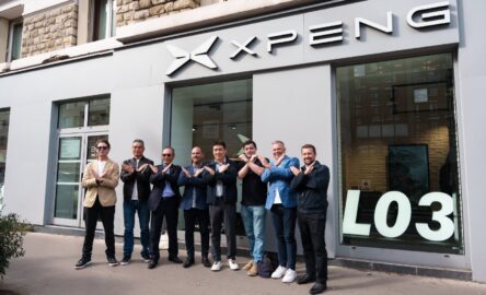 A group poses with crossed arms outside an Xpeng showroom with an L03 window display.